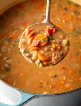 Top down view soup made with 15 beans and veggies in a large cooking pot. A metal ladle is showing a spoonful to camera.