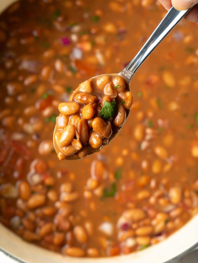 Spoon with a heap of beans on it with more in the pot in the background.