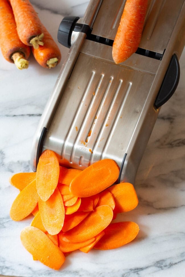 healthy chips Carrots being sliced on a mandolin slicer.