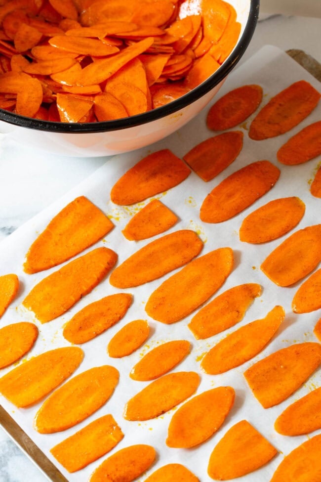 healthy chips Thinly sliced carrots placed on a baking sheet lined with parchment paper before being baked.
