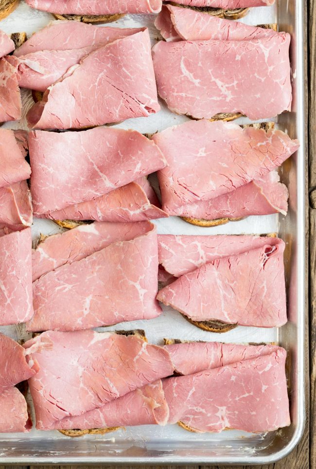 Bread assembled with corned beef slices on a sheet pan.