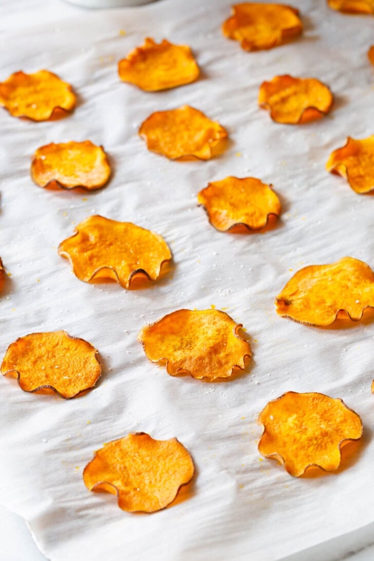 Sweet potato chips after being baked on a baking sheet lined with parchment paper.