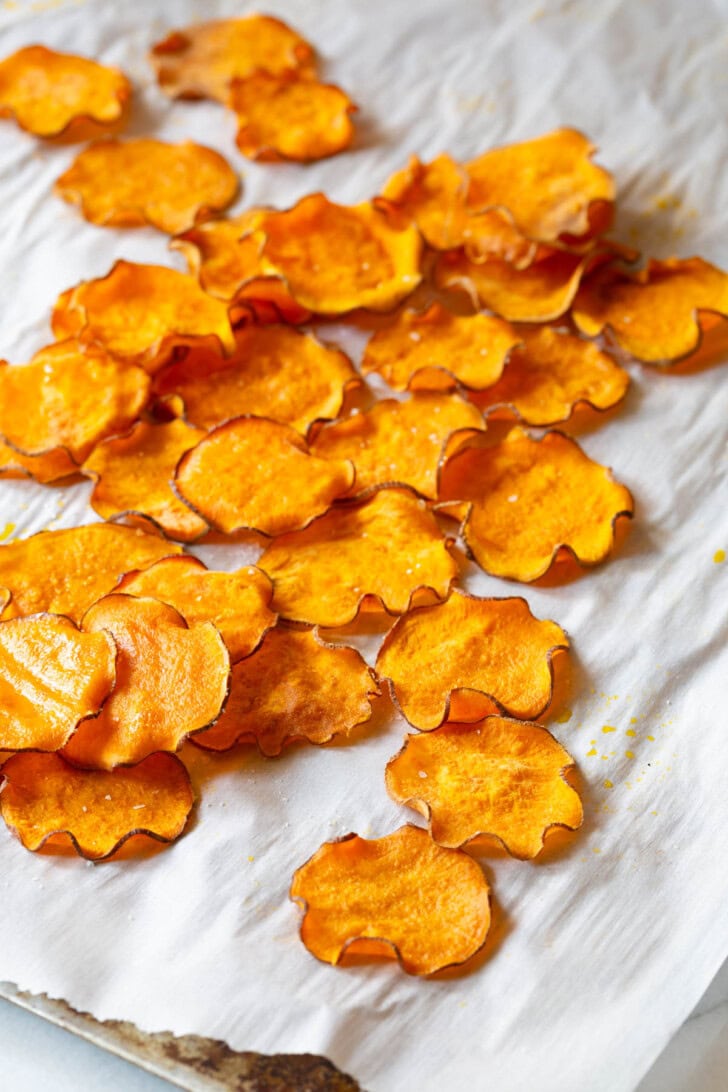 Baked sweet potato chips spread out on some parchment paper.
