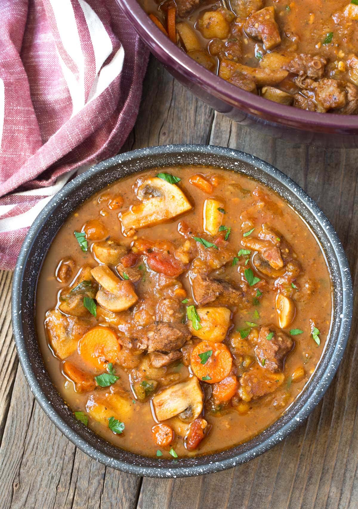 Beef Stew Recipe #ASpicyPerspective #BeefStew #BeefStewRecipe #Stew #StewRecipe #Beef #Crockpot #InstantPot #Stovetop #BeefStewCrockpot #SlowCookerBeefStew #BestBeefStew #HowtoMakeBeefStew Bowl of easy beef stew with a pot of more beef stew in the background.