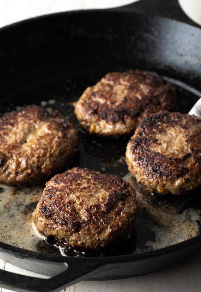 Hamburger patties being cooked in a cast iron skillet.