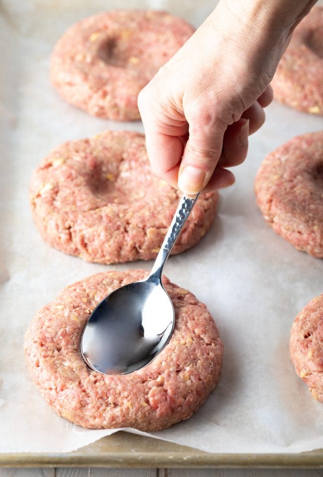 Hand using a spoon to make a small dent in the hamburger patties before cooking.