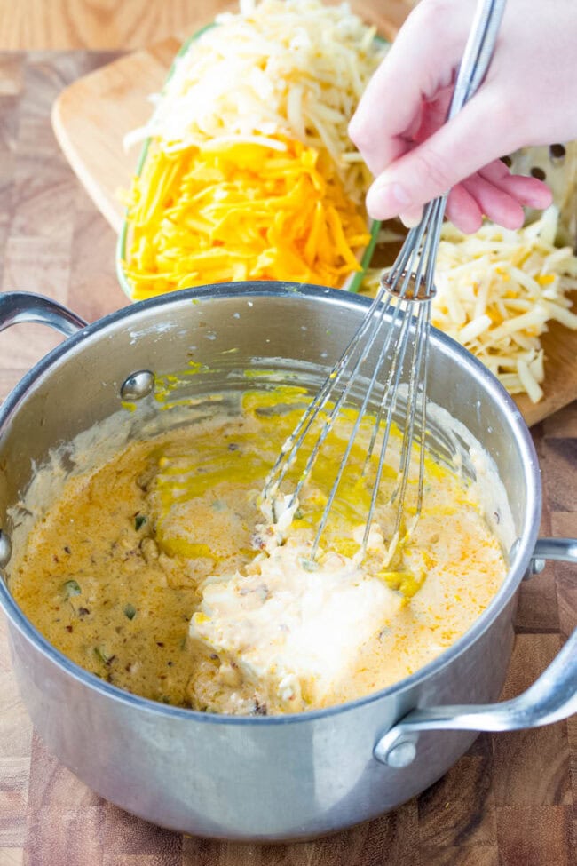 How to make queso cheese sauce. The Best Queso recipe is easy and flavorful, with sharp and smoky notes. Start dipping those tortilla chips! #ASpicyPerspective #queso #cheese #dip Hand mixing queso ingredients in pot with a whisk.