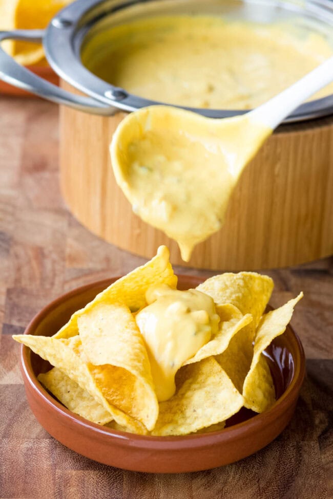 Cheese sauce makes or breaks any nacho recipe. The Best Queso recipe is easy and flavorful, with sharp and smoky notes. Start dipping those tortilla chips! #ASpicyPerspective #queso #cheese #dip Cheese sauce dripping over tortilla chips with a ladle.