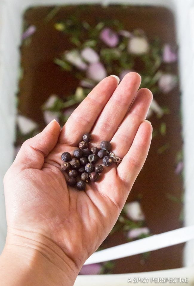 Hand with peppercorns in it holding them over a cooler filled with turkey brine.