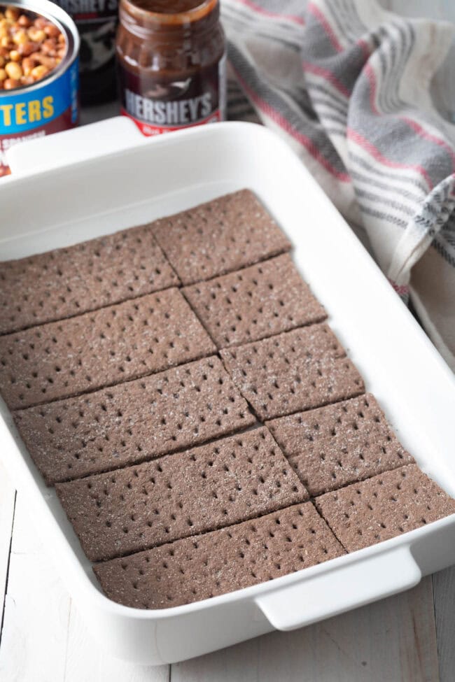 First layer of chocolate graham crackers in a white baking dish.