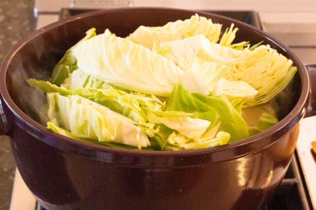 How to Make Irish Cabbage and Bacon Recipe for Saint Patrick's Day! #ASpicyPerspective #IrishCabbageBacon #Irish #Cabbage #Bacon #StPatricksDay #Dinner #SideDish Cabbage cooking in a large pot on the stove.