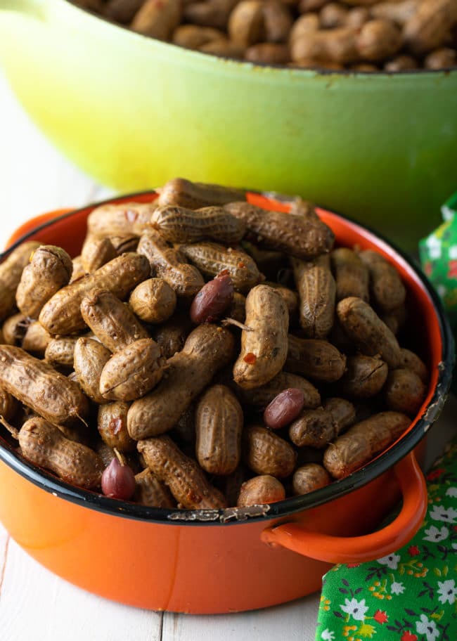 Boiled peanuts in an orange pot next to a larger pot with more peanuts in it.