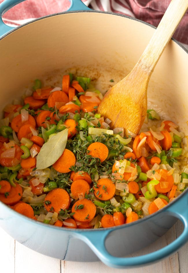 Vegetables sautรฉing in a soup pot with a wooden spoon.