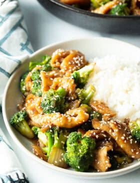 White shallow bowl with serving of Chinese chicken and broccoli with white rice.