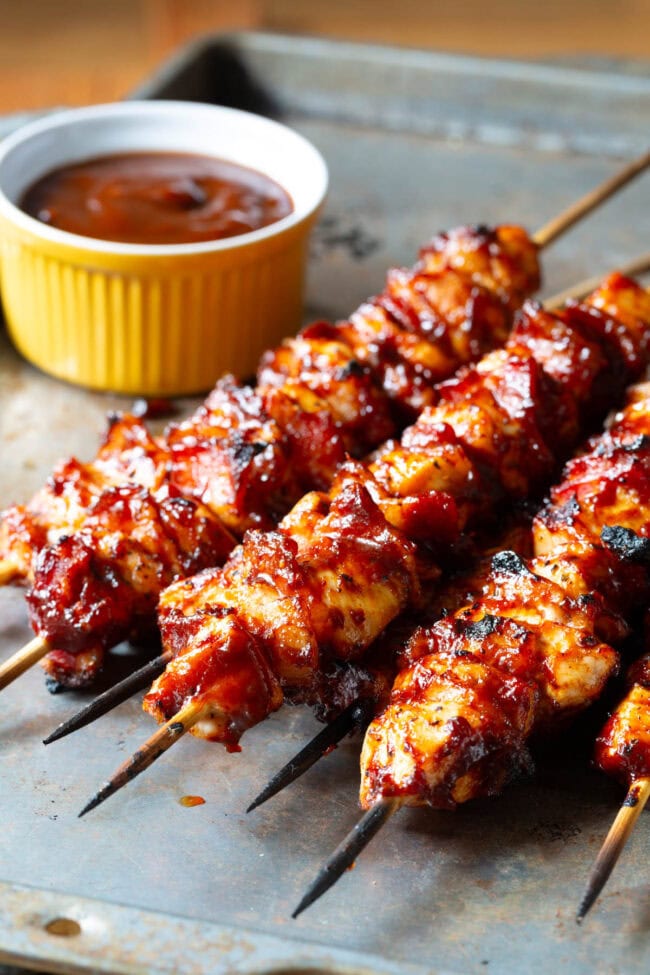Chicken Skewers Recipe #ASpicyPerspective #Chicken #Bacon #BBQ #Chipotle #Skewers #ChickenSkewers #BBQChicken #ChickenSkewersRecipe #BBQSkewers #ChipotleChicken #Grill #Summer Chicken BBQ Skewers Recipe on baking tray with sauce