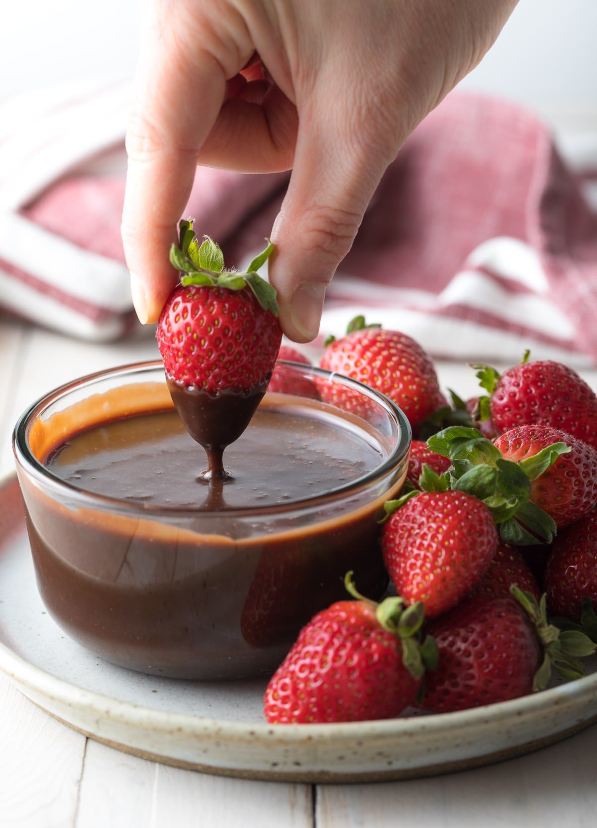 Hand dipping a fresh strawberry into chocolate fondue.