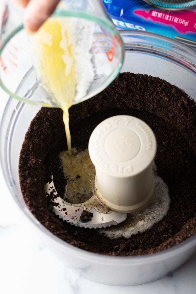 adding butter to the crushed oreos in a food processor
