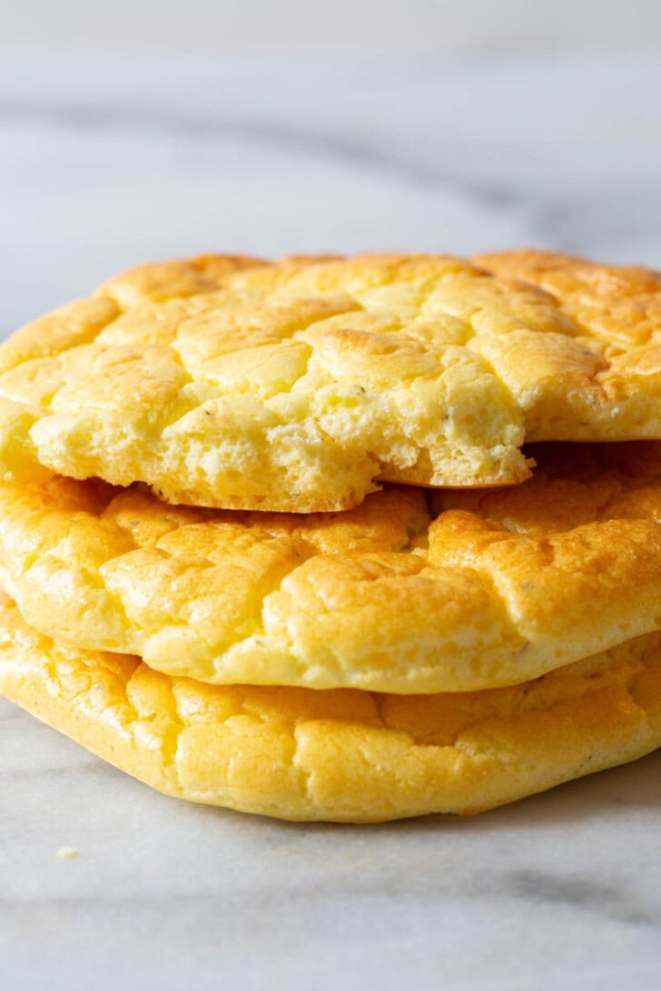 Cloud Bread Recipe #ASpicyPerspective #LowCarb #GlutenFree #GrainFree #Keto #CloudBread #CloudBreadRecipe #KetoCloudBread #NoCarbBread Pieces of cloud bread stacked on top of each other with one of them ripped in half to show the inside.