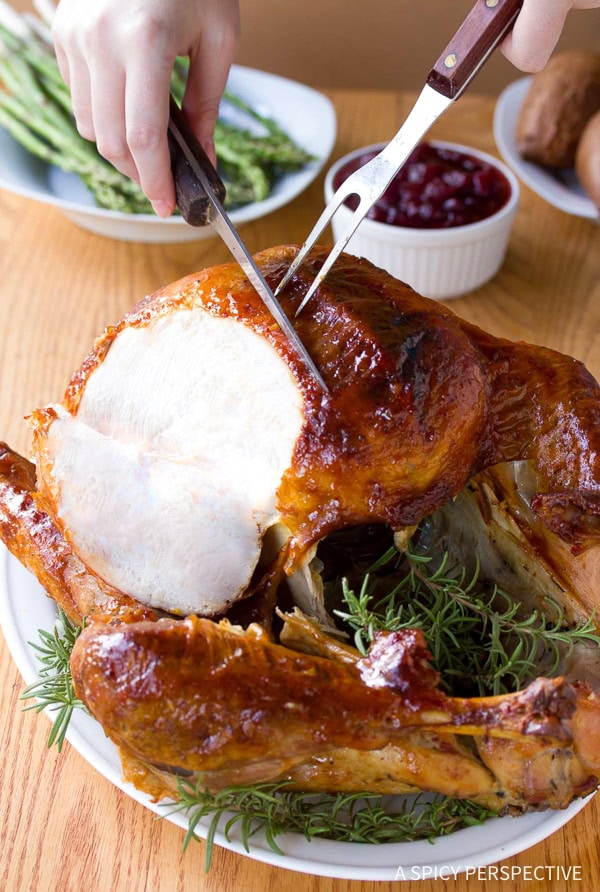 cranberry-jalapeno-honey Hands carving into a whole roast turkey on a serving platter lined with herbs.