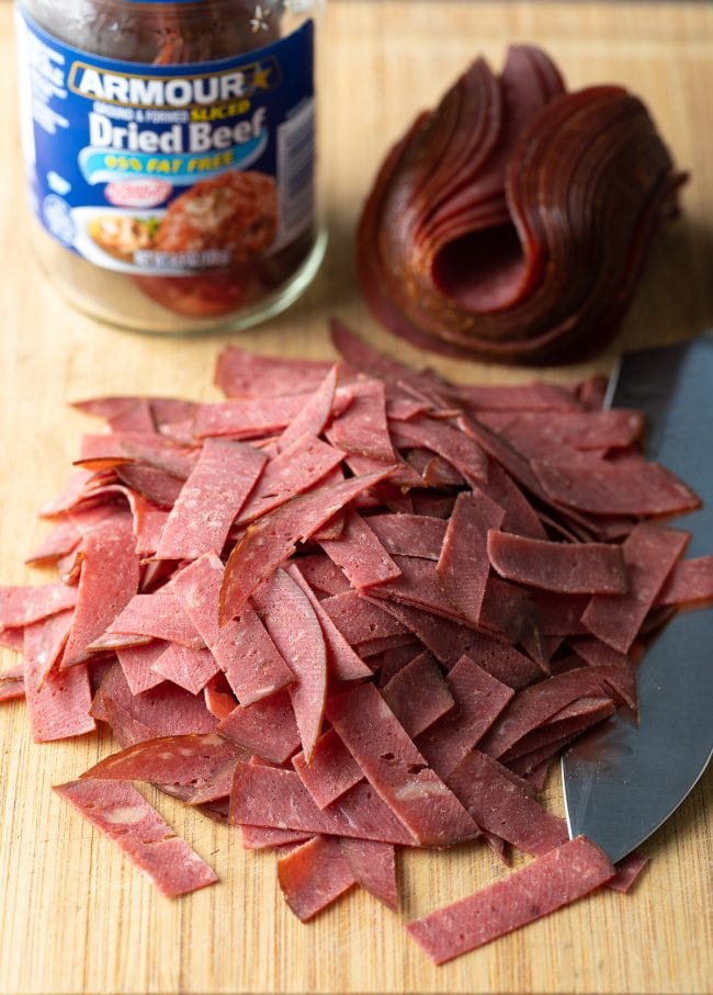 Buddig dried beef sliced into strips on a wooden cutting board.