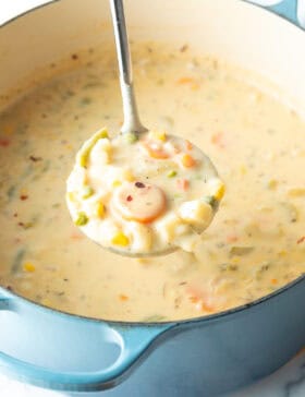 Large cooking pot with creamy vegetable soup, with a ladle showing a scoop to camera.