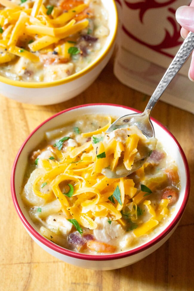 Potato Soup Recipe #ASpicyPerspective #CrockpotPotatoSoup #Chicken #Potato #Soup #Healthy #SlowCooker #Crockpot #PotatoSoup #PotatoSoupRecipe #DairyFree #GlutenFree #LowFat Crockpot Potato soup in a bowl with a hand holding a spoon scooping up a bite.