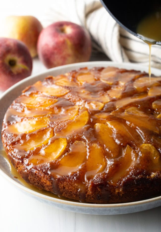 Upside down apple cake on a serving plate with whiskey sauce being poured on top.