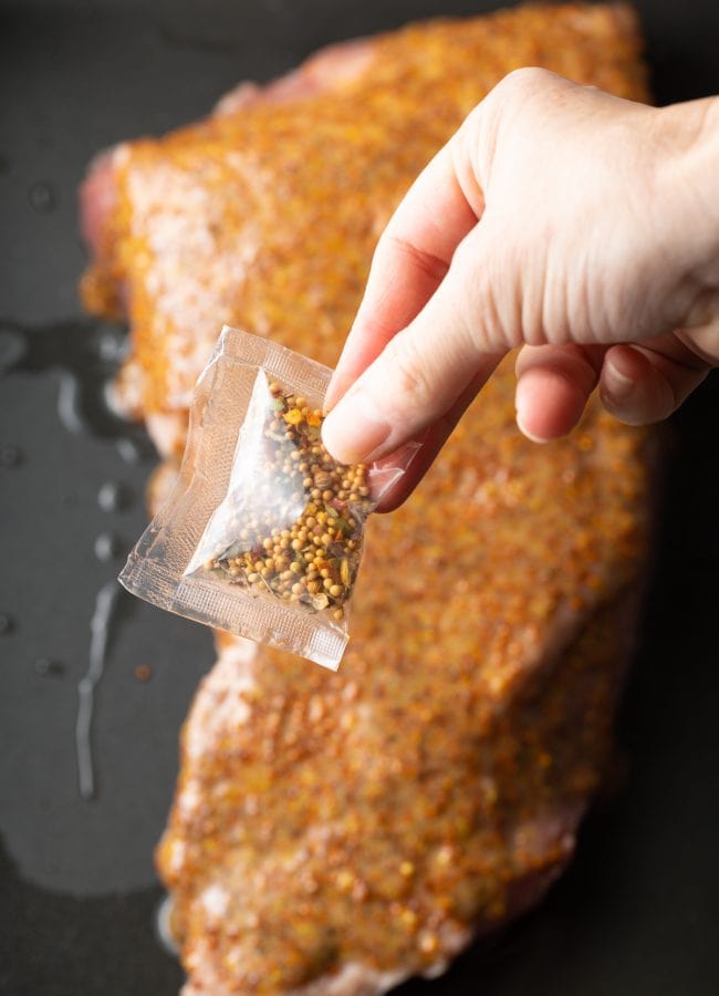 Hand holding the packed of corned beef seasoning above the raw corned beef brisket.