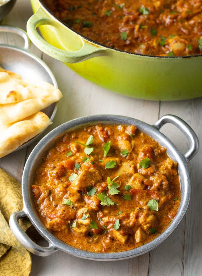 Easy Chicken Madras Curry in a silver bowl next to naan bread and a dutch oven.