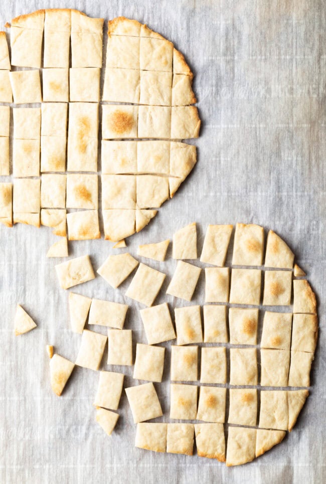 Two pieces of unleavened bread laying on a gray background. Each large oval of bread has been sliced into small squares.