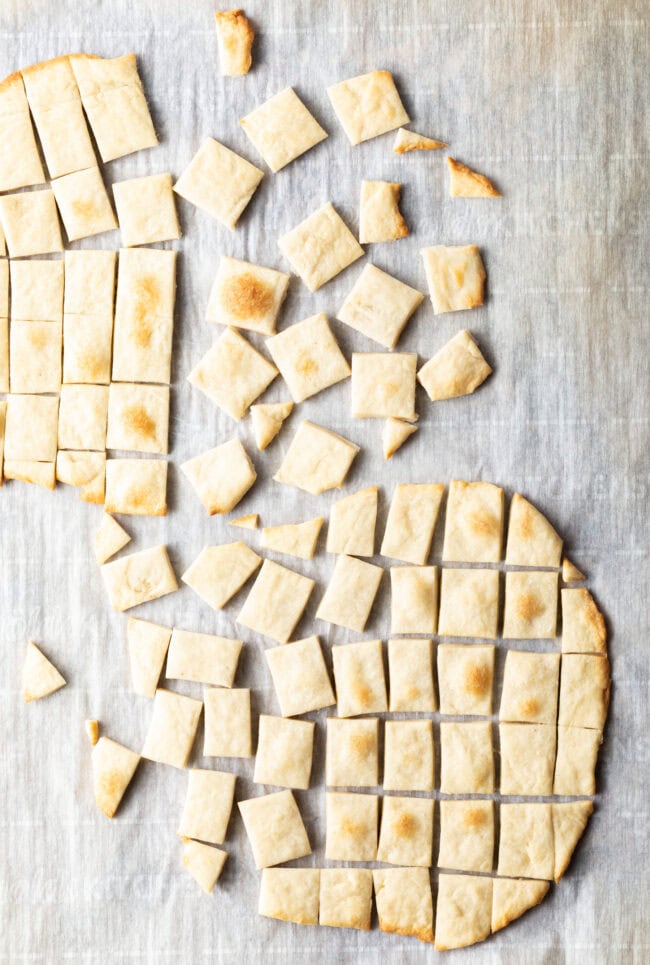 Two pieces of unleavened bread laying on a gray background. Each large oval of bread has been sliced into small squares.