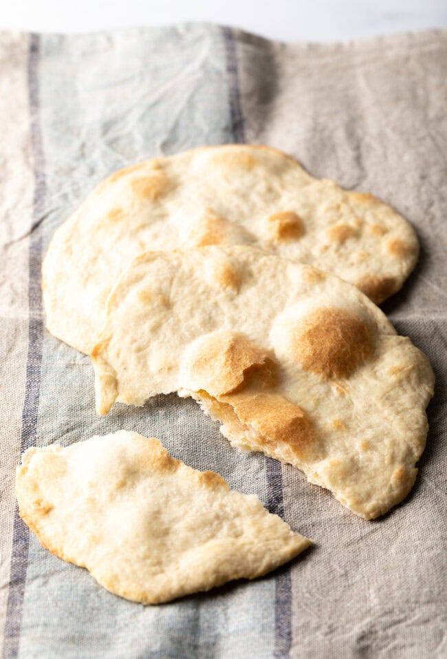 Two pieces of unleavened bread laying on a gray background. One bread has been split into two pieces.