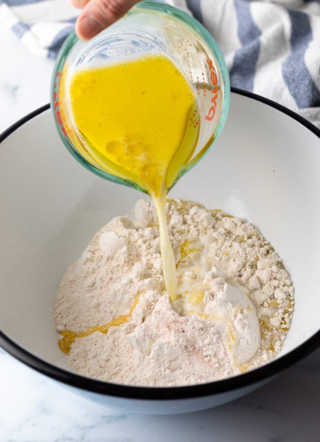 Adding melted butter to the flour mixture in a large white mixing bowl.