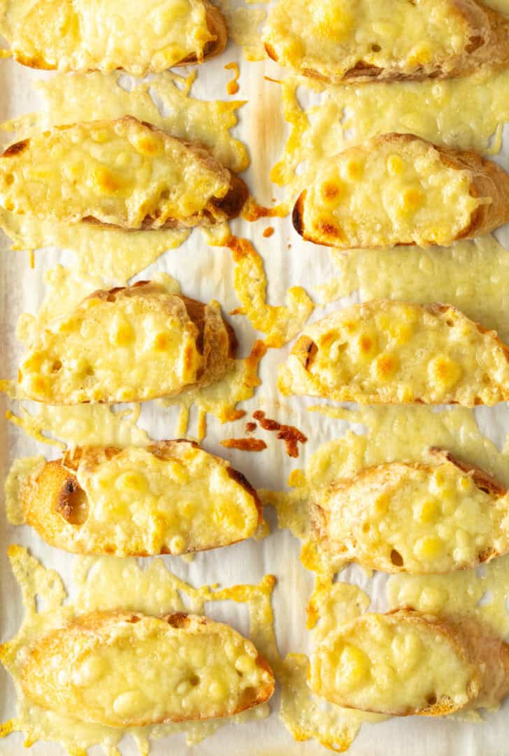 10 slices of baguette on a baking sheet, topped with melted cheese.