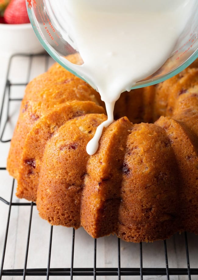 Hand pouring the glaze over the top of the strawberry cake.