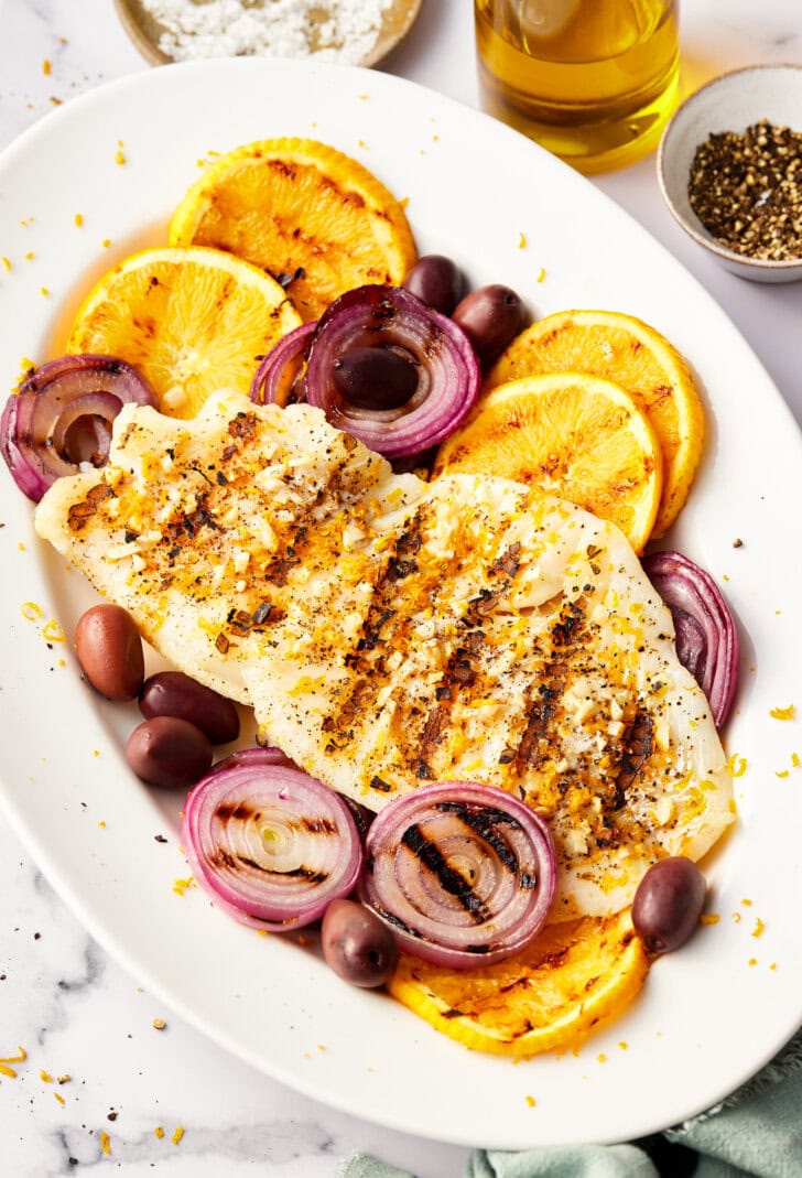 Grilled grouper on a serving platter with grilled onions, oranges and kalamata olives.