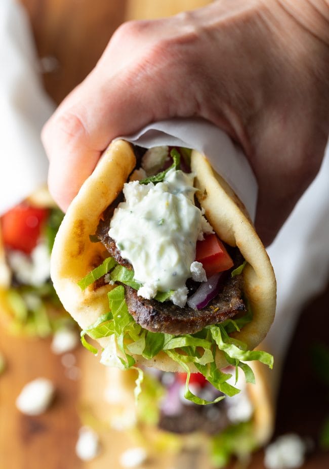 Hand holding a lamb gyro recipe with tzatziki sauce on top.
