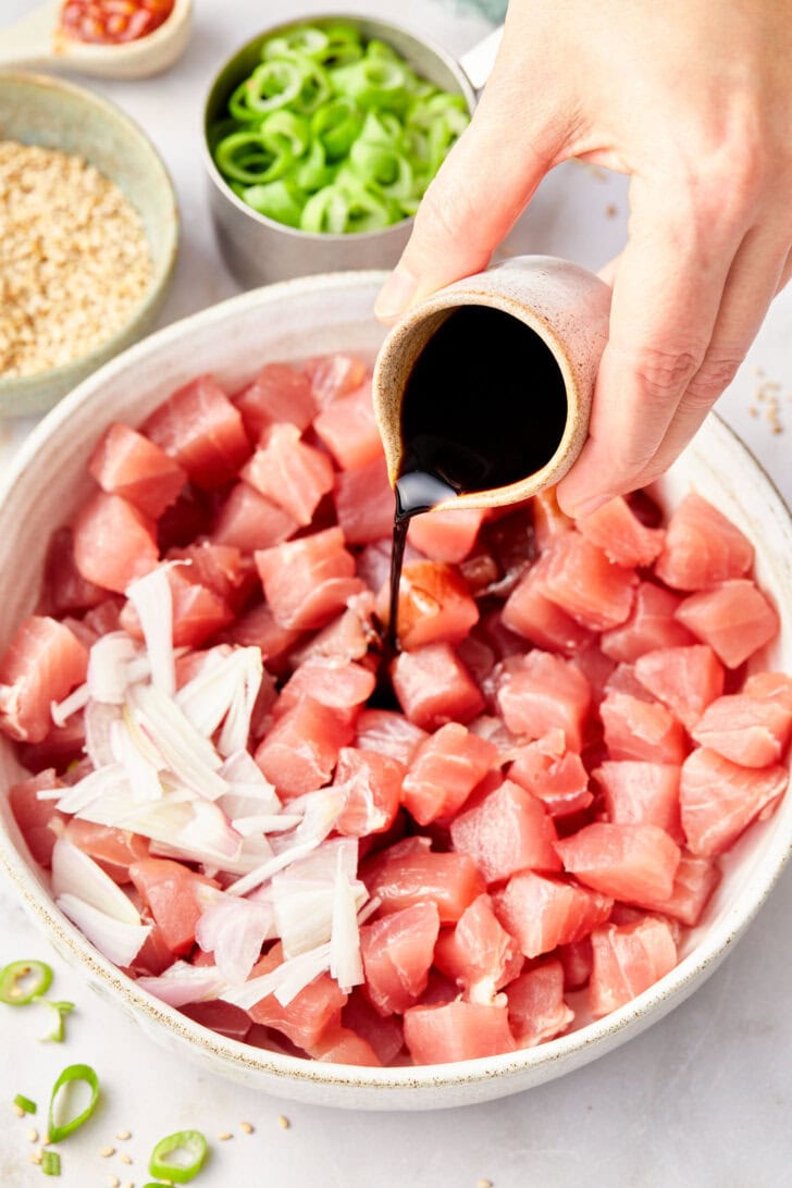 Hand pouring soy sauce into the bowl with tuna and shallots.