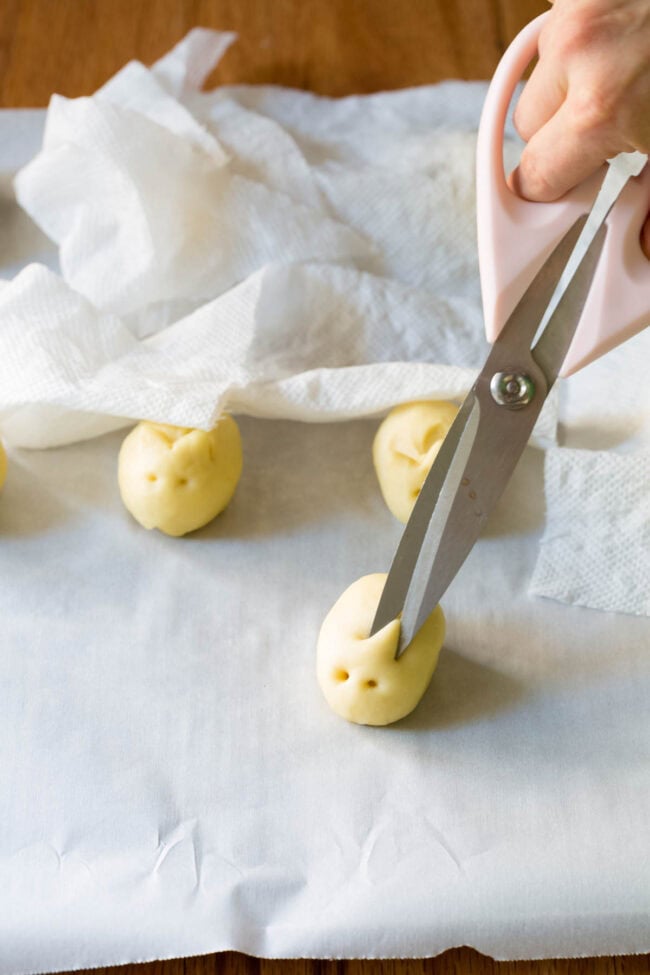 Hand holding scissors to make bunny ears in the yeasted dough.