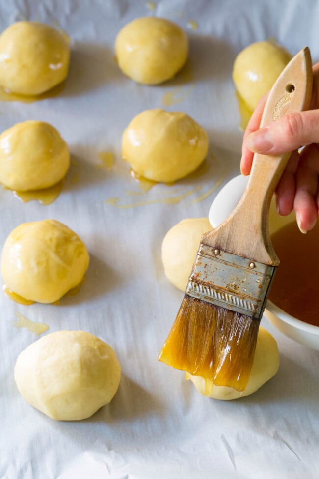 Roll dough in balls on a baking sheet with a hand brushing butter on top.