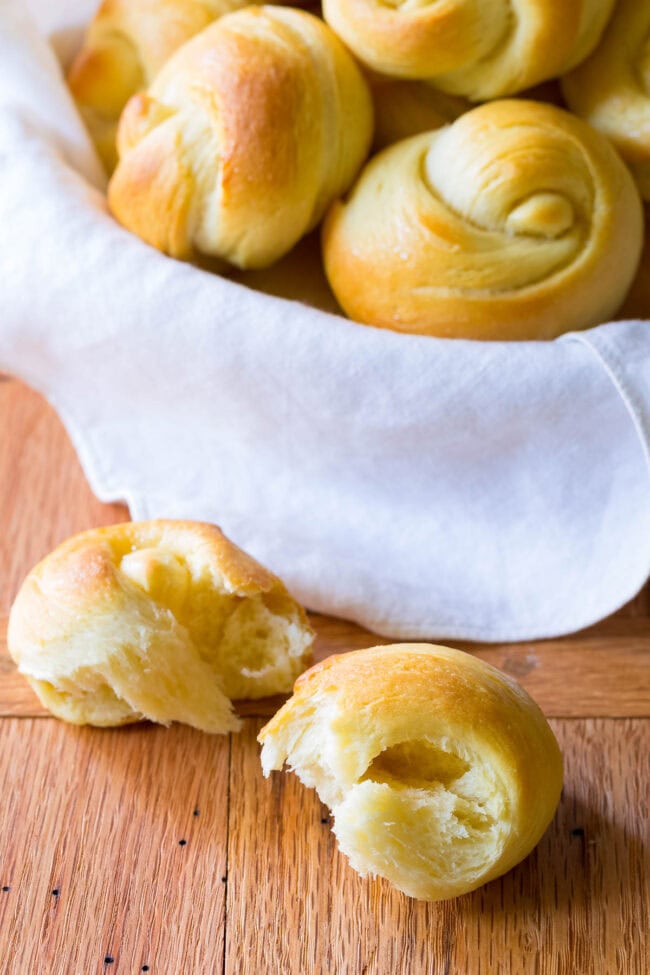 Basket of yeast roll recipe with one in front of the basket ripped in half to show the inside.