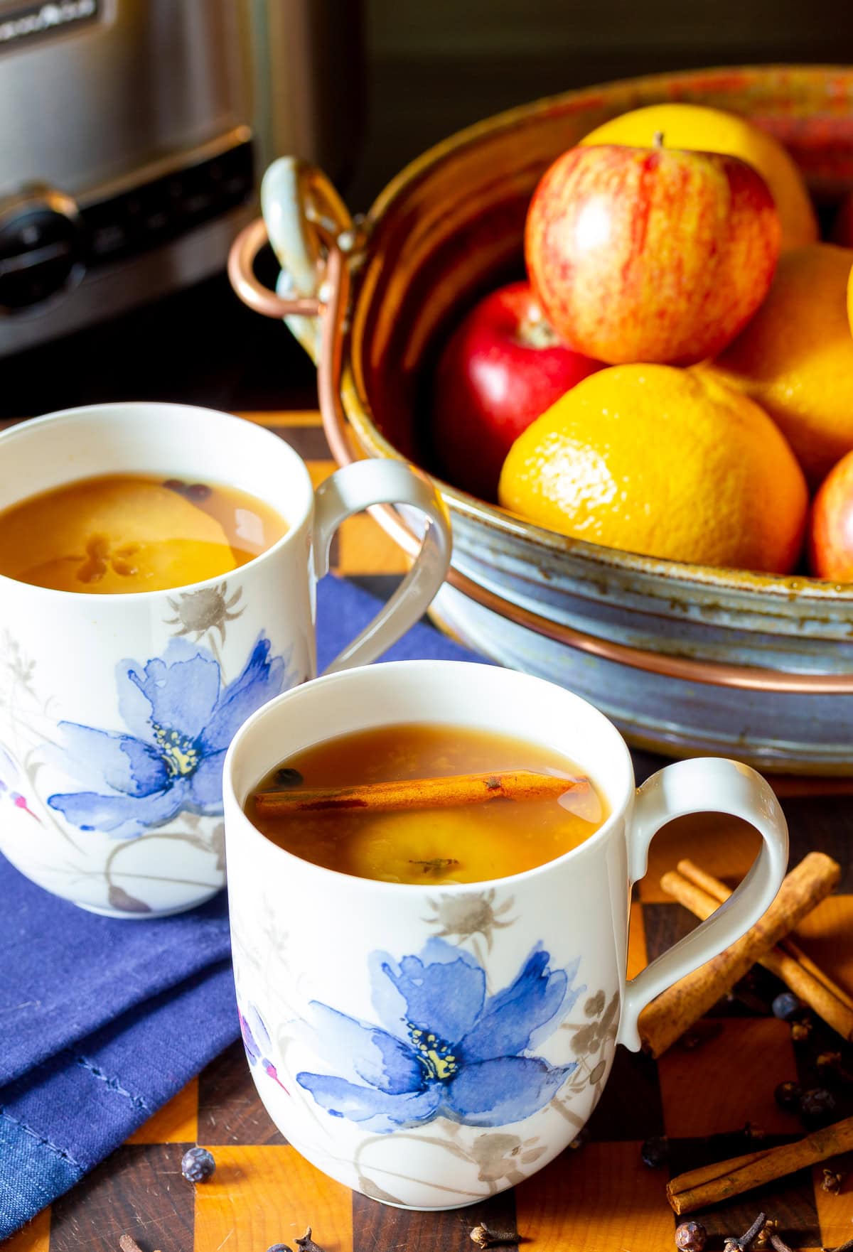 hot-apple-cider Two mugs of apple cider next to a bowl of oranges and apples.