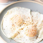 Two cooked eggs over easy on a light blue plate, sprinkled with spices.