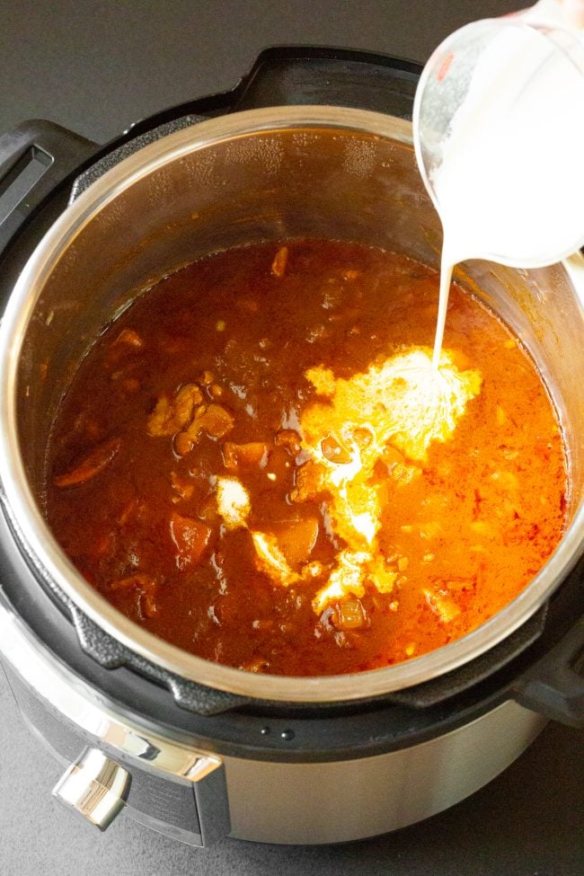 indian chicken curry with cream being poured into it.
