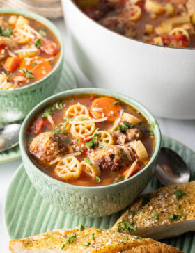 Green bowl of Italian meatball soup loaded with wheel shaped pasta, sliced carrots, in a tomato broth.