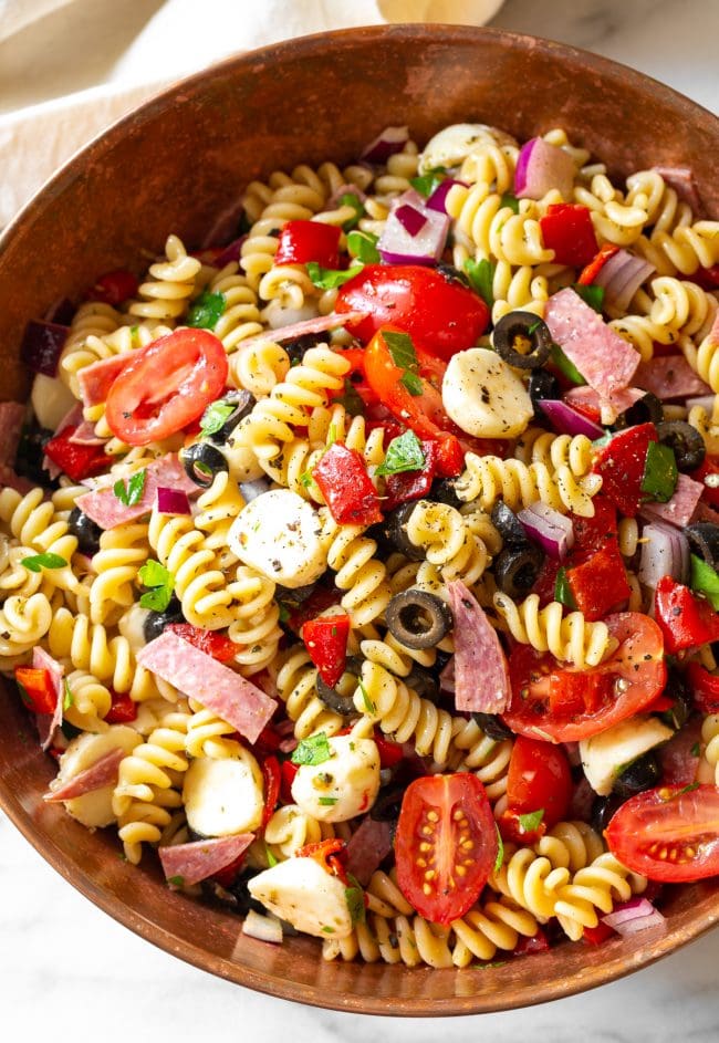 Pasta Salad #ASpicyPerspective #PastaSalad #PastaSaladRecipe #ItalianPastaSalad #Italian #Salad #BestPastaSalad #Spring #Summer Noodles, veggies, salami, cheese and olives with dressing in a large bowl.