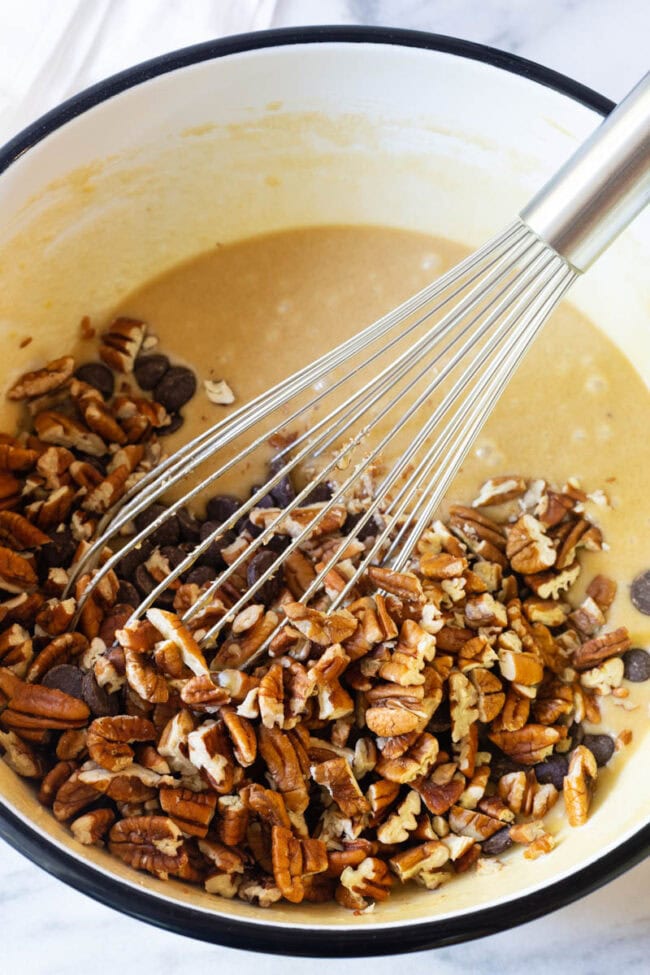 pecans Whisking chopped nuts and chocolate chips into an eggy batter in a large mixing bowl.