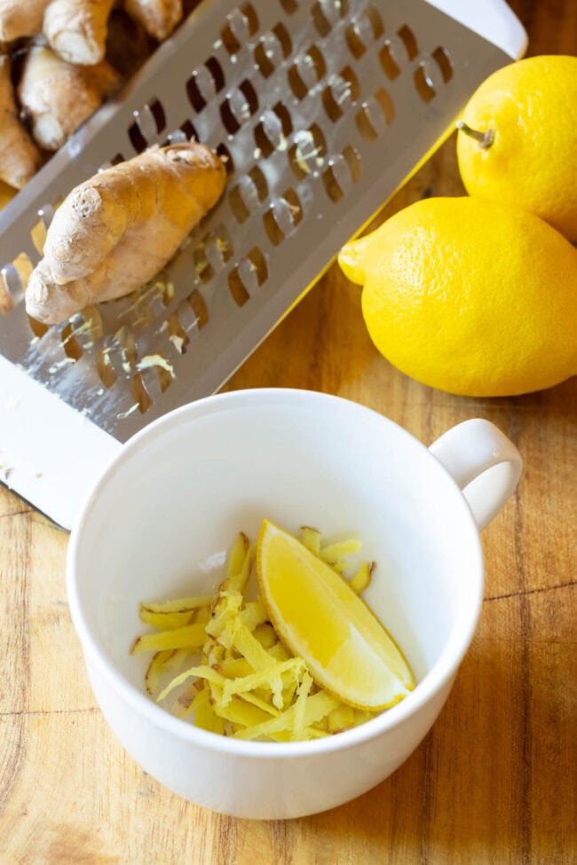 Making Lemon Ginger Detox Tea - Grated ginger and lemon wedge in a white mug.