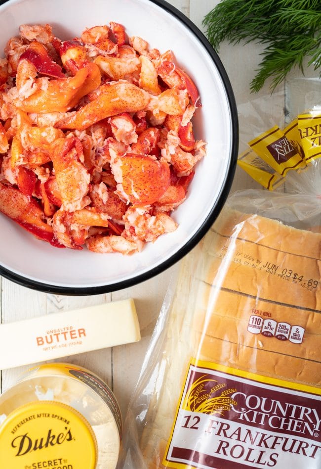 Lobster meat in a bowl with butter and rolls next to them. 