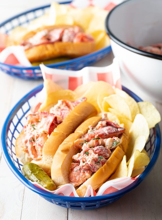 Lobster rolls in serving baskets served with chips and pickles. 